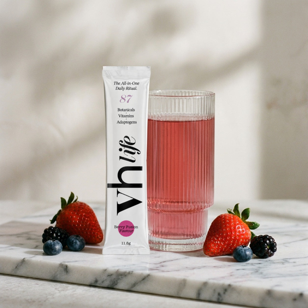 A vh life Berry sachet standing beside a glass of the berry drink in soft morning light