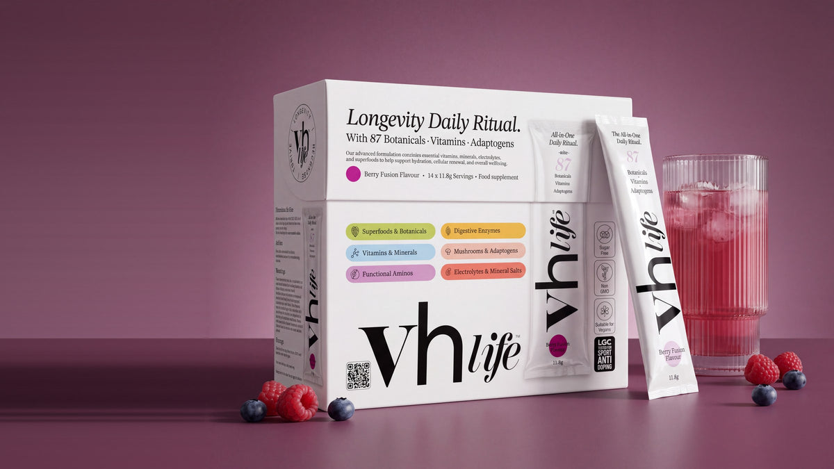 The VH Life box, a berry sachet and a glass of the berry drink with berries on a plum surface