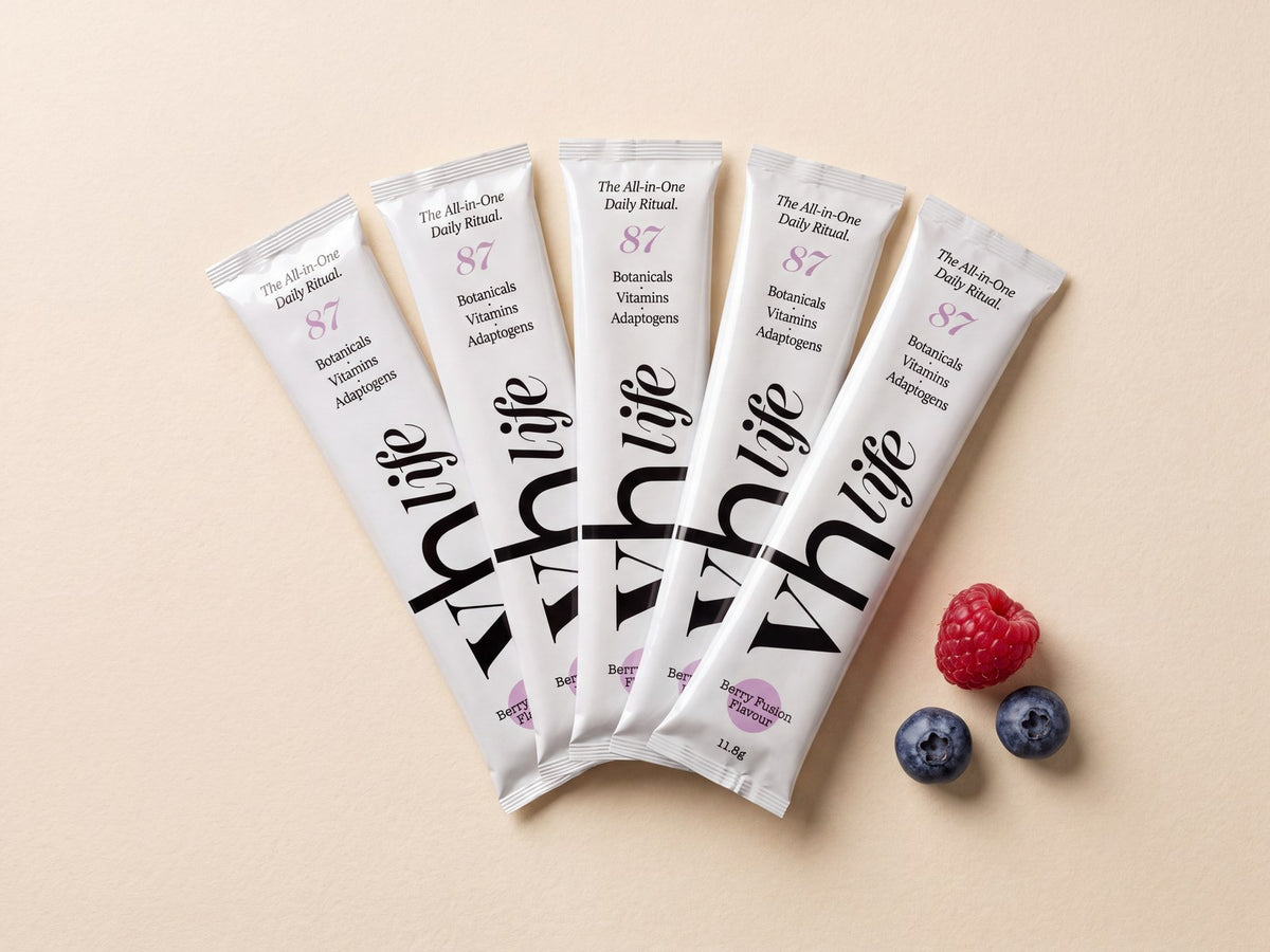 Five VH Life berry sachets fanned out on a cream surface with a few berries